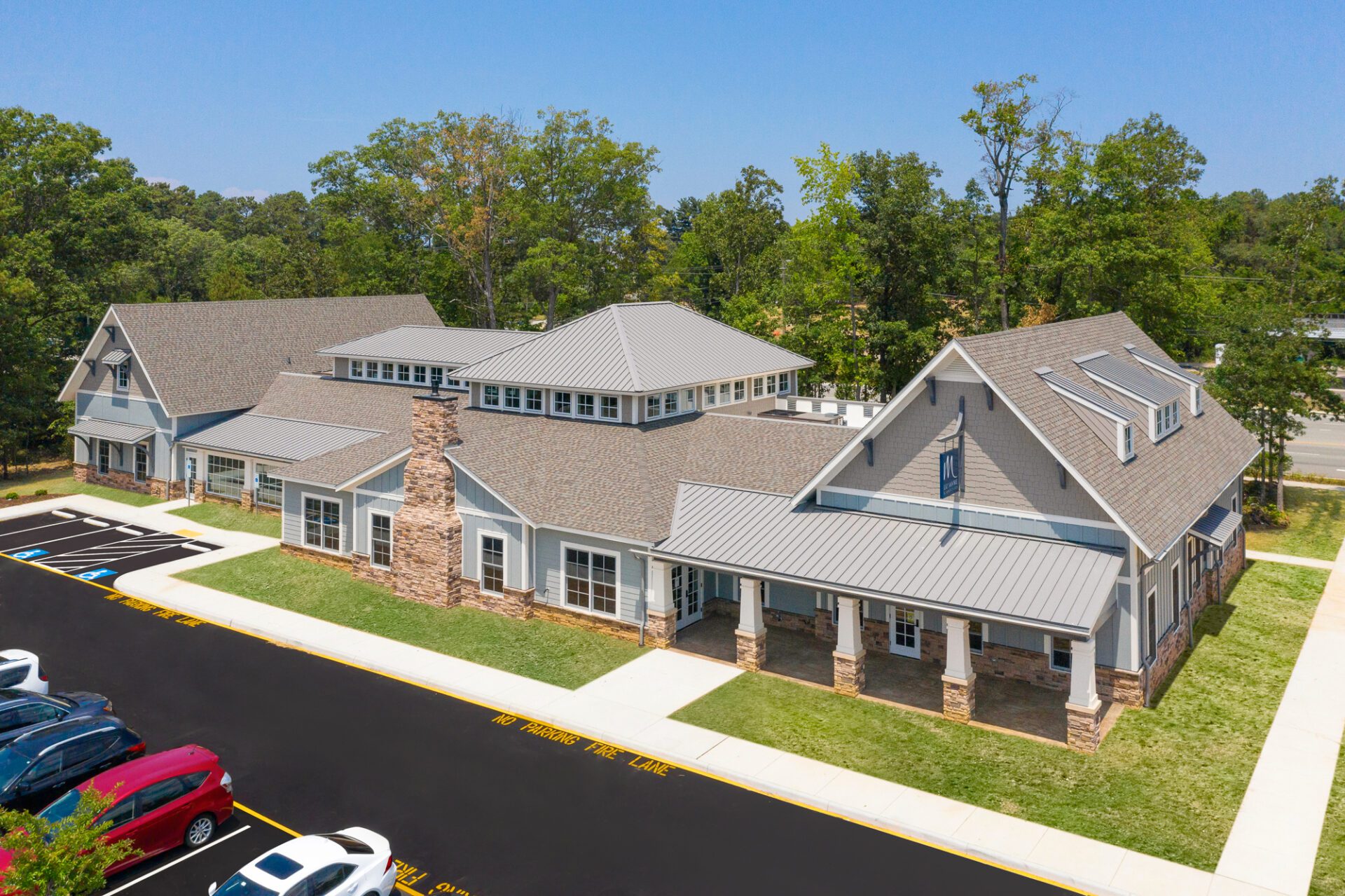 1 Aerial view of a modern suburban building with gray roofing and stone accents, surrounded by a parking lot