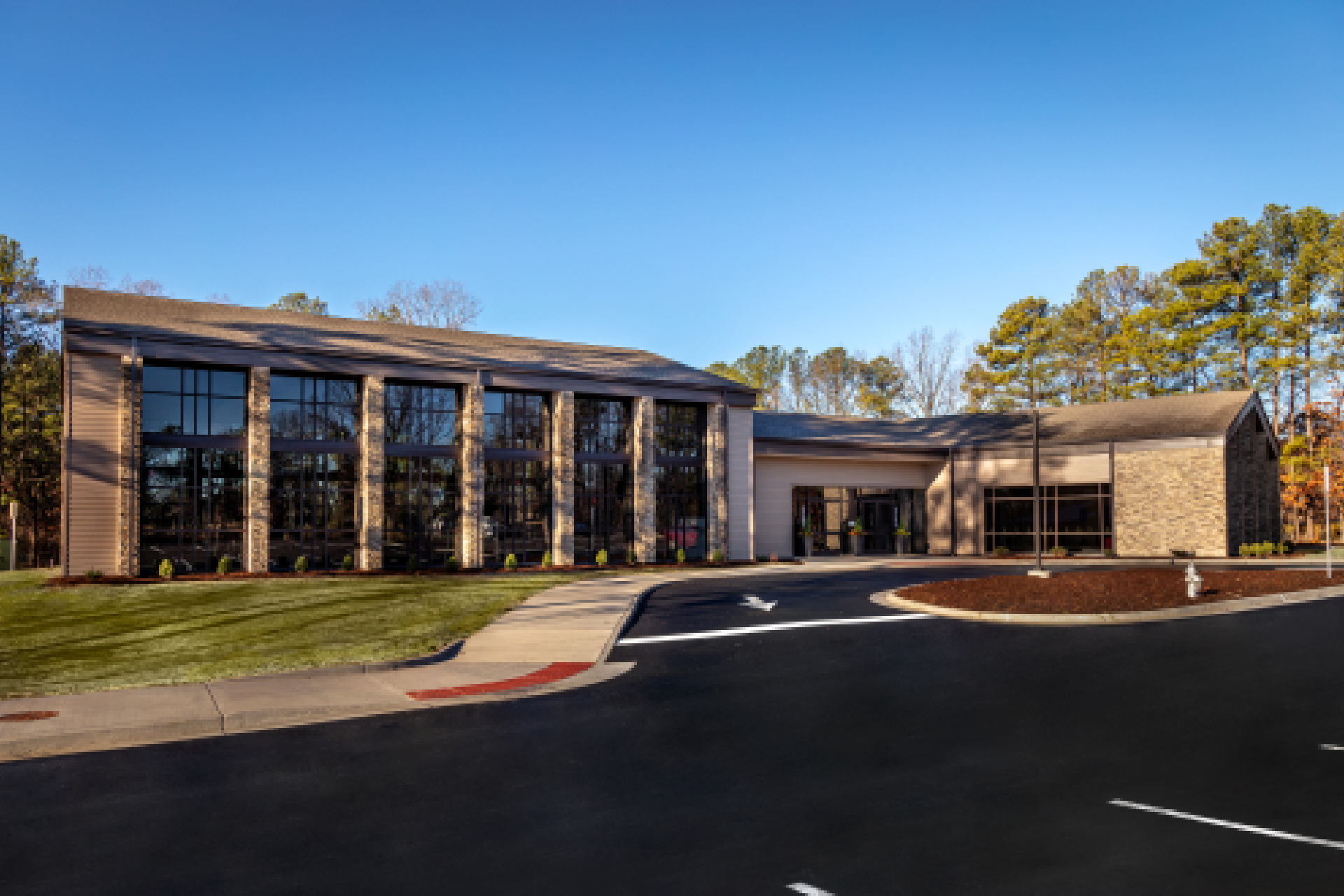New Project (31) Aerial view of a modern suburban building with gray roofing and stone accents, surrounded by a parking lot